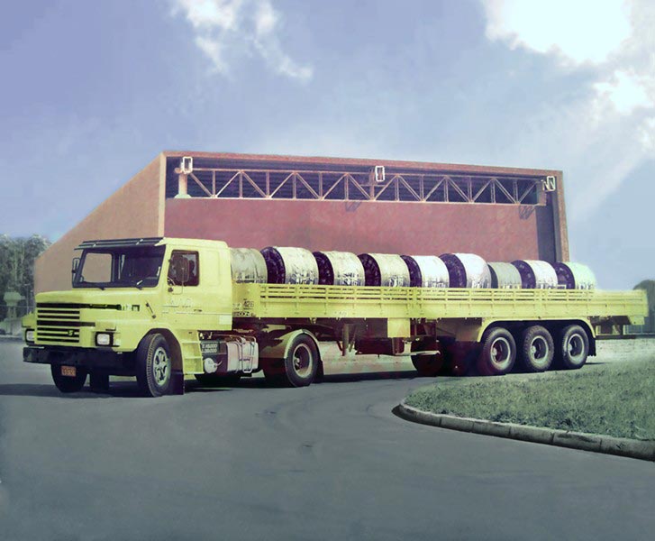 Carreta histórica A.N.R carregando bobinas de aço siderúrgicas em frente ao galpão da empresa